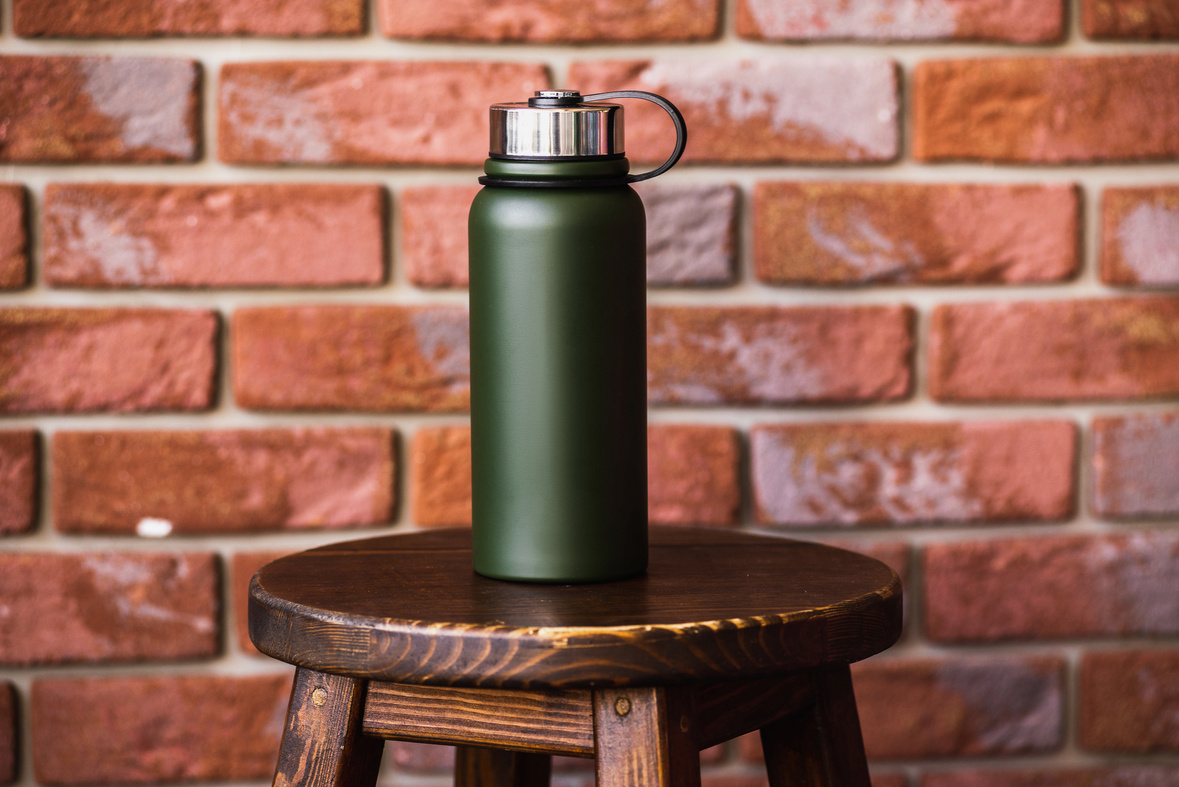 Thermos bottle near brick wall background. Coffee or tea reusable bottle container. Thermos travel tumbler. Insulated drink container.